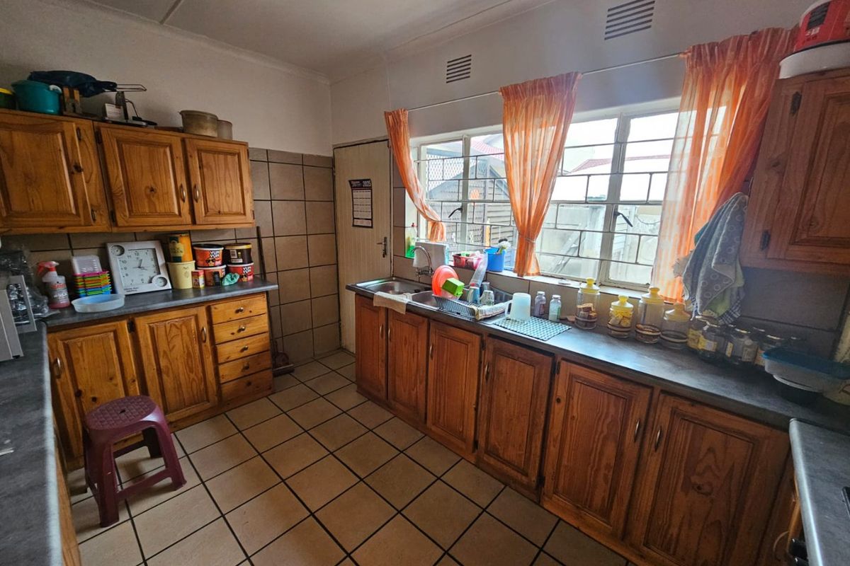 A functional kitchen featuring traditional wooden cabinetry, tiled flooring, and a stainless steel sink, offering a classic layout with potential for modern updates.