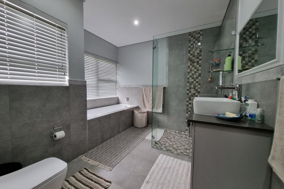 Modern bathroom featuring a built-in bathtub, glass-enclosed shower, vessel sink vanity, and contemporary grey tile finishes throughout.