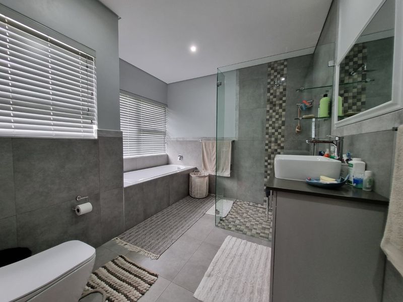 Modern bathroom featuring a built-in bathtub, glass-enclosed shower, vessel sink vanity, and contemporary grey tile finishes throughout.