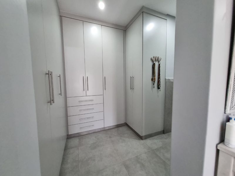 A modern walk-in dressing area featuring extensive white built-in cabinetry, sleek hardware, and neutral floor tiles.