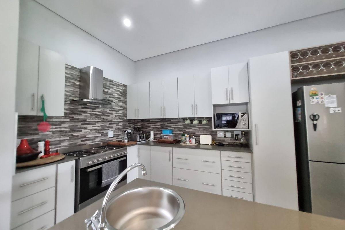 Modern kitchen featuring white cabinetry, stone countertops, a stainless steel gas stove with extractor, and a convenient island with an undermount sink.