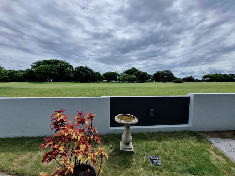 A scenic view overlooking a large, well-maintained green lawn and mature trees, framed by a modern boundary wall.