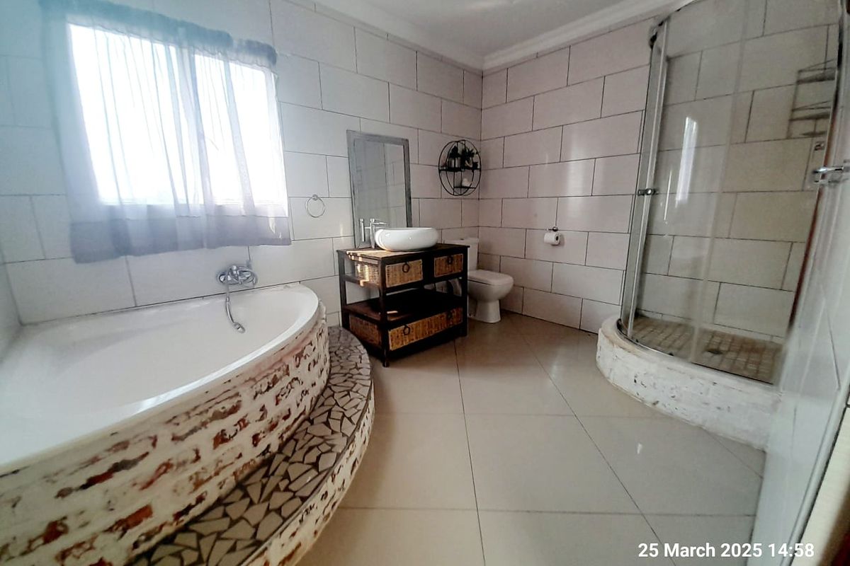 A spacious bathroom featuring a raised corner bathtub with mosaic detailing, a separate glass-enclosed shower, and a vanity unit.