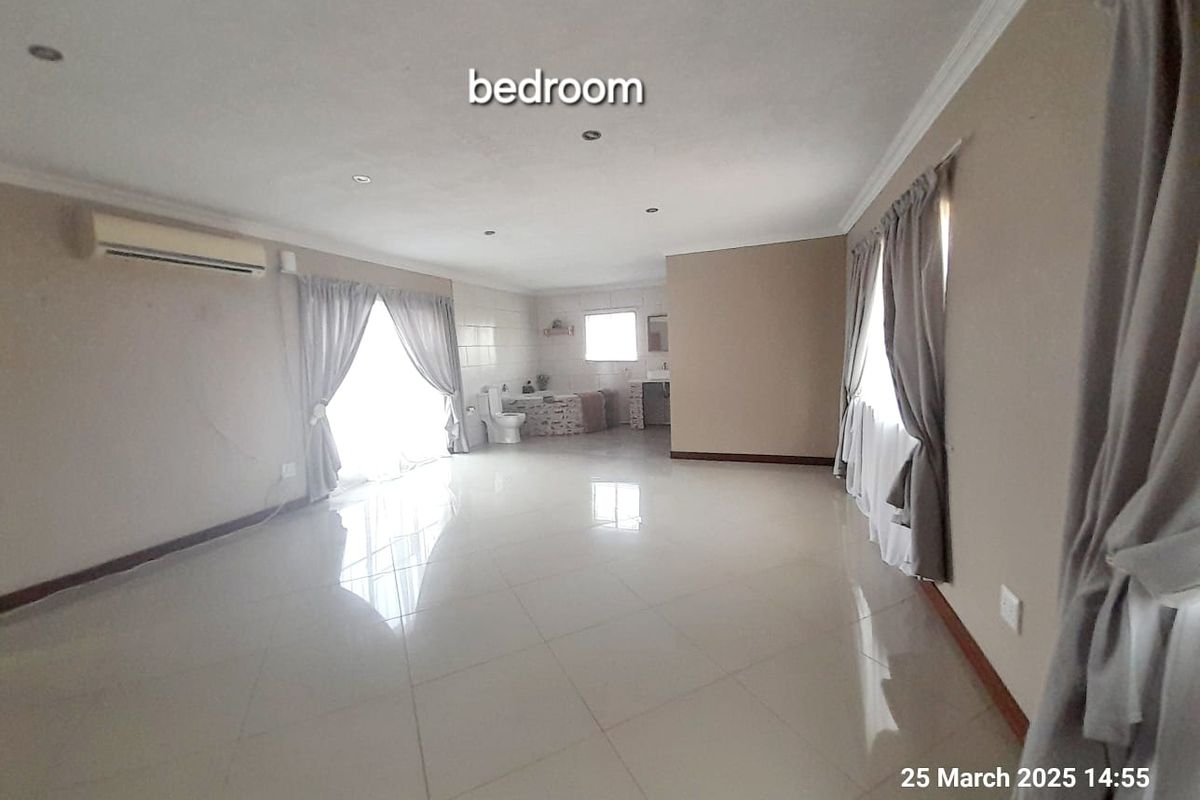 Spacious open-plan bedroom featuring tiled flooring, recessed ceiling lighting, and an integrated en-suite bathroom area with a bathtub and vanity.