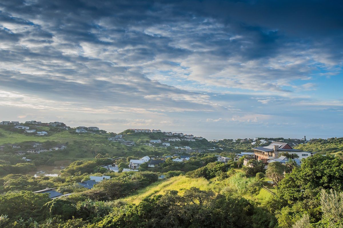 An elevated aerial view of a residential estate nestled within a lush, green landscape with distant coastal views.