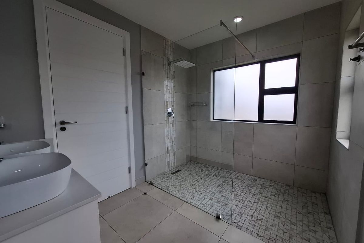 Modern bathroom featuring a spacious walk-in shower with glass enclosure, mosaic tile flooring, and dual vanity basins.