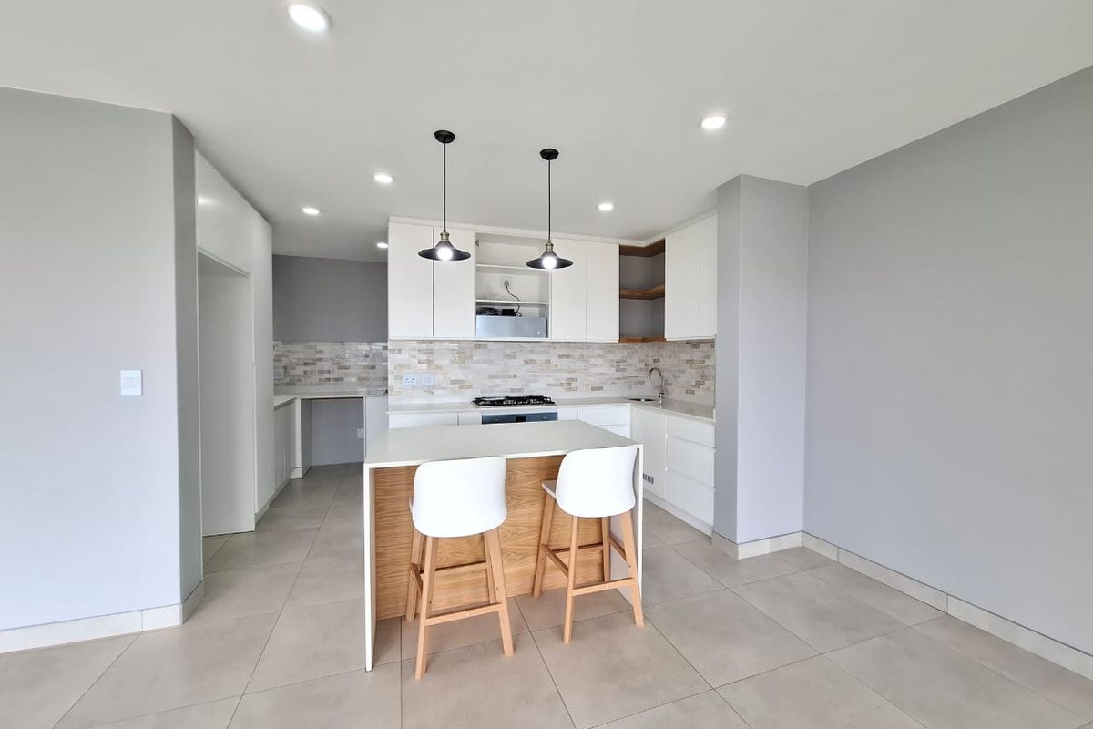 Modern open-plan kitchen featuring white cabinetry, stone-look backsplash, a central island with breakfast bar, and recessed ceiling lighting.
