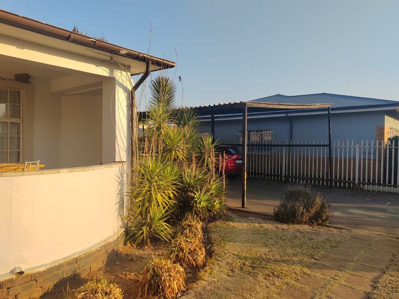 Front exterior view of the house featuring a covered patio, paved driveway, and a metal carport structure.