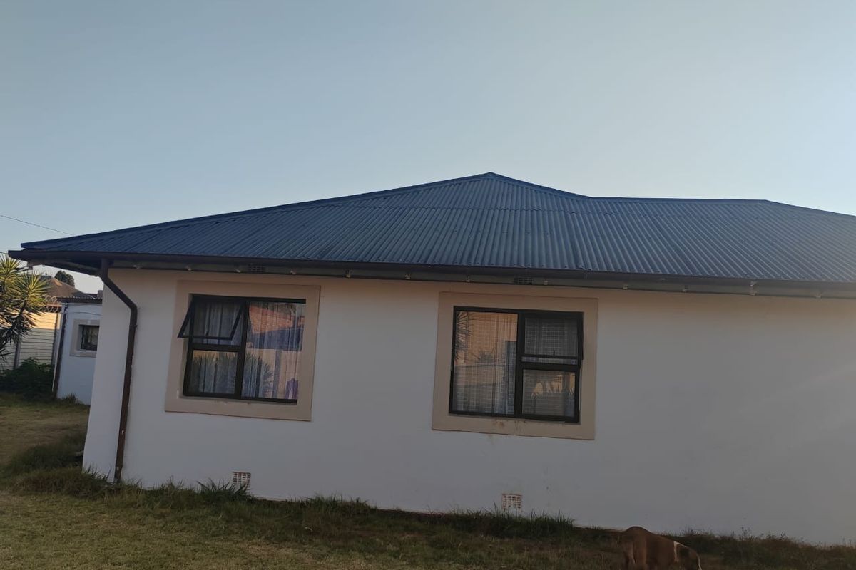 A view of the rear exterior elevation featuring a corrugated metal roof, white rendered walls, and dark aluminium window frames.