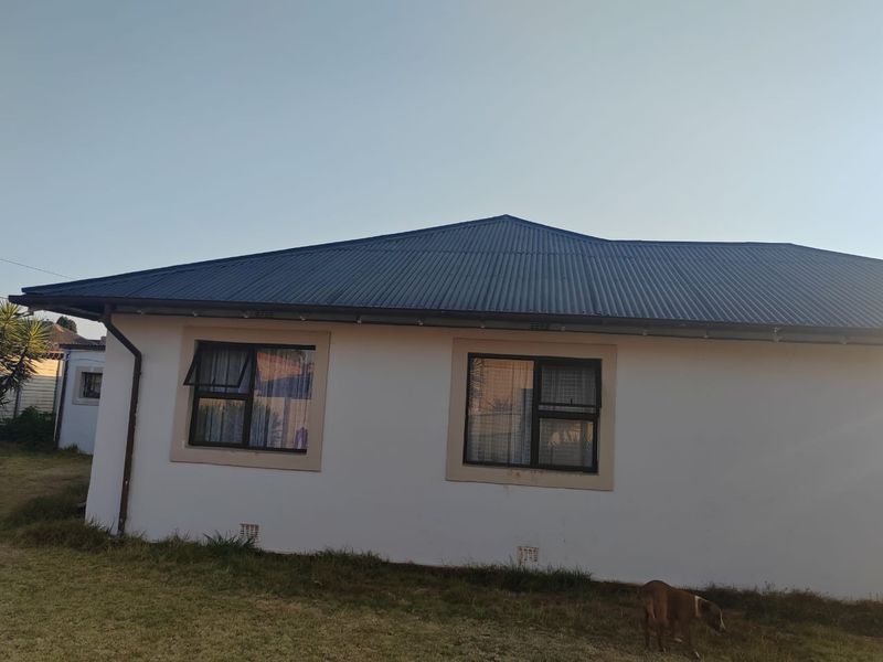 A view of the rear exterior elevation featuring a corrugated metal roof, white rendered walls, and dark aluminium window frames.