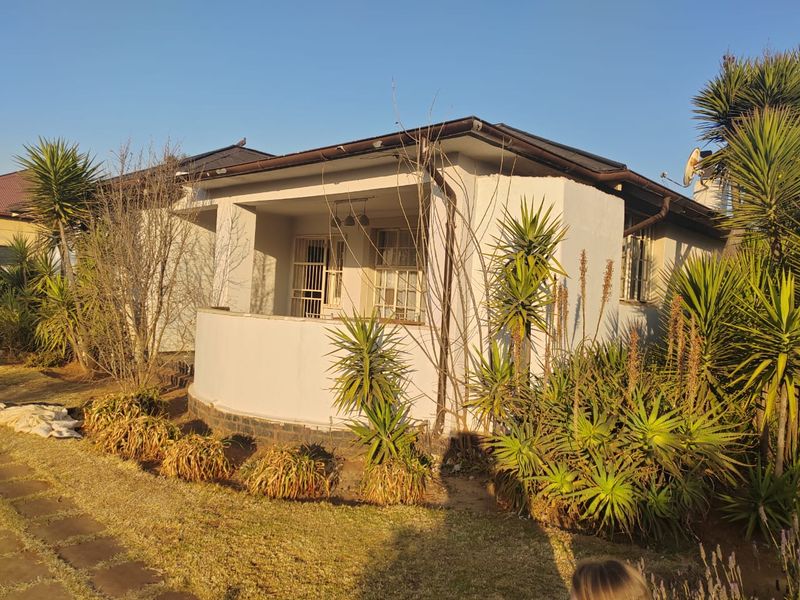 Front view of a single-story house featuring a covered porch, security gates, and established garden landscaping.