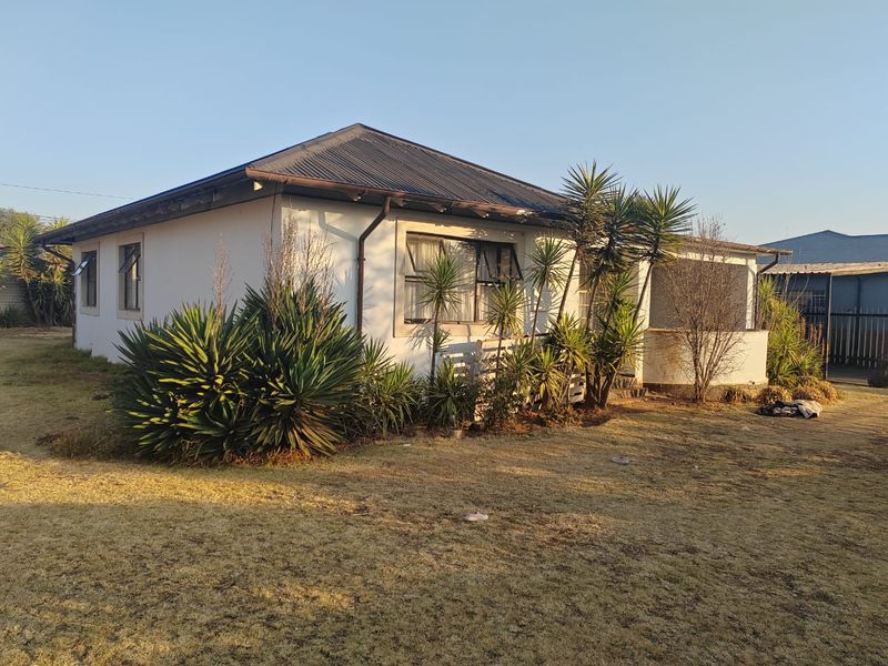 A single-story residential house featuring a corrugated metal roof, plastered exterior walls, and a covered entrance porch, set on a large plot.