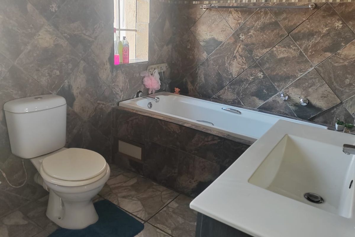 A functional bathroom featuring a built-in bathtub, toilet, and vanity basin with dark stone-look wall tiling.