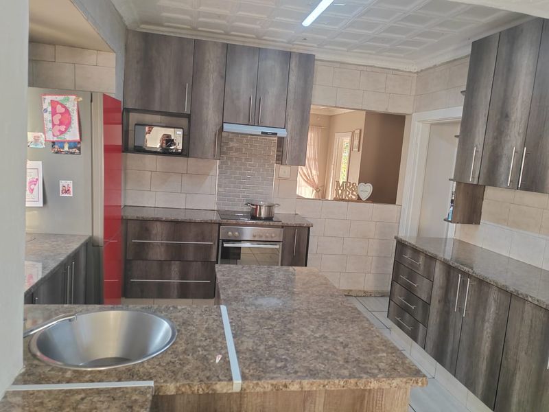 A functional kitchen featuring dark wood-grain cabinetry, granite countertops, a built-in oven and hob, and a central island with a stainless steel sink.