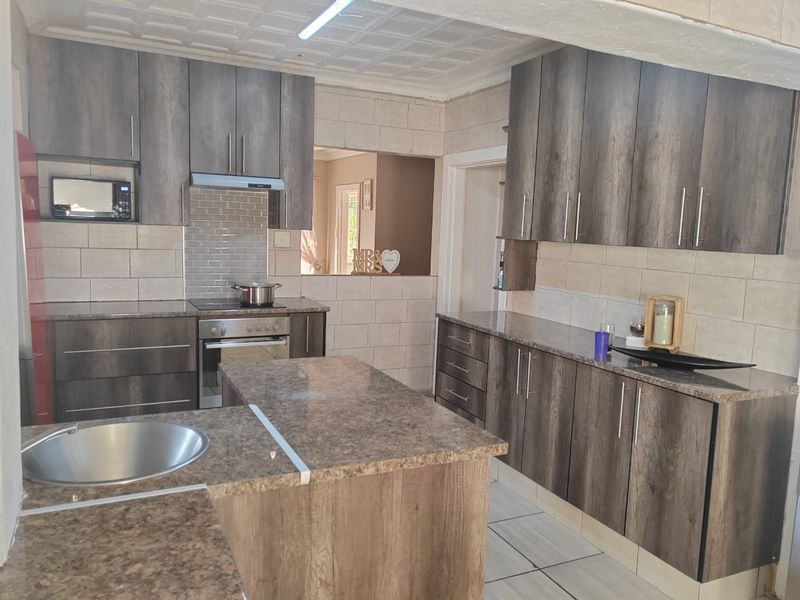 Modernized kitchen featuring dark wood-grain cabinetry, granite countertops, built-in oven, hob, and extractor fan with a functional layout and tiled finishes.
