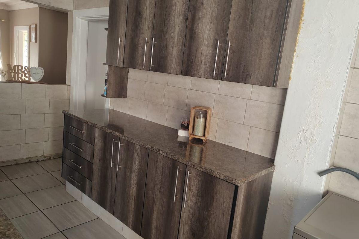 A kitchen area featuring dark wood-look cabinetry, granite countertops, and tiled backsplash, currently showing signs of incomplete wall finishing and plaster damage.