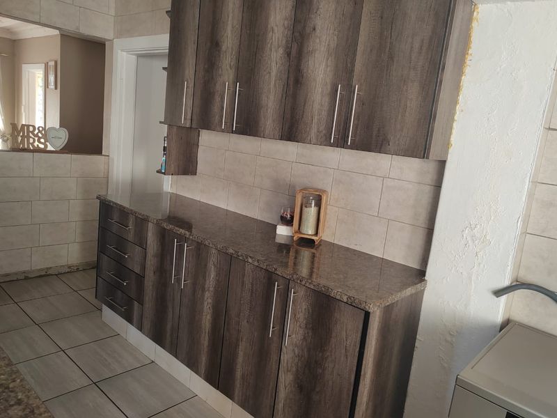 A kitchen area featuring dark wood-look cabinetry, granite countertops, and tiled backsplash, currently showing signs of incomplete wall finishing and plaster damage.