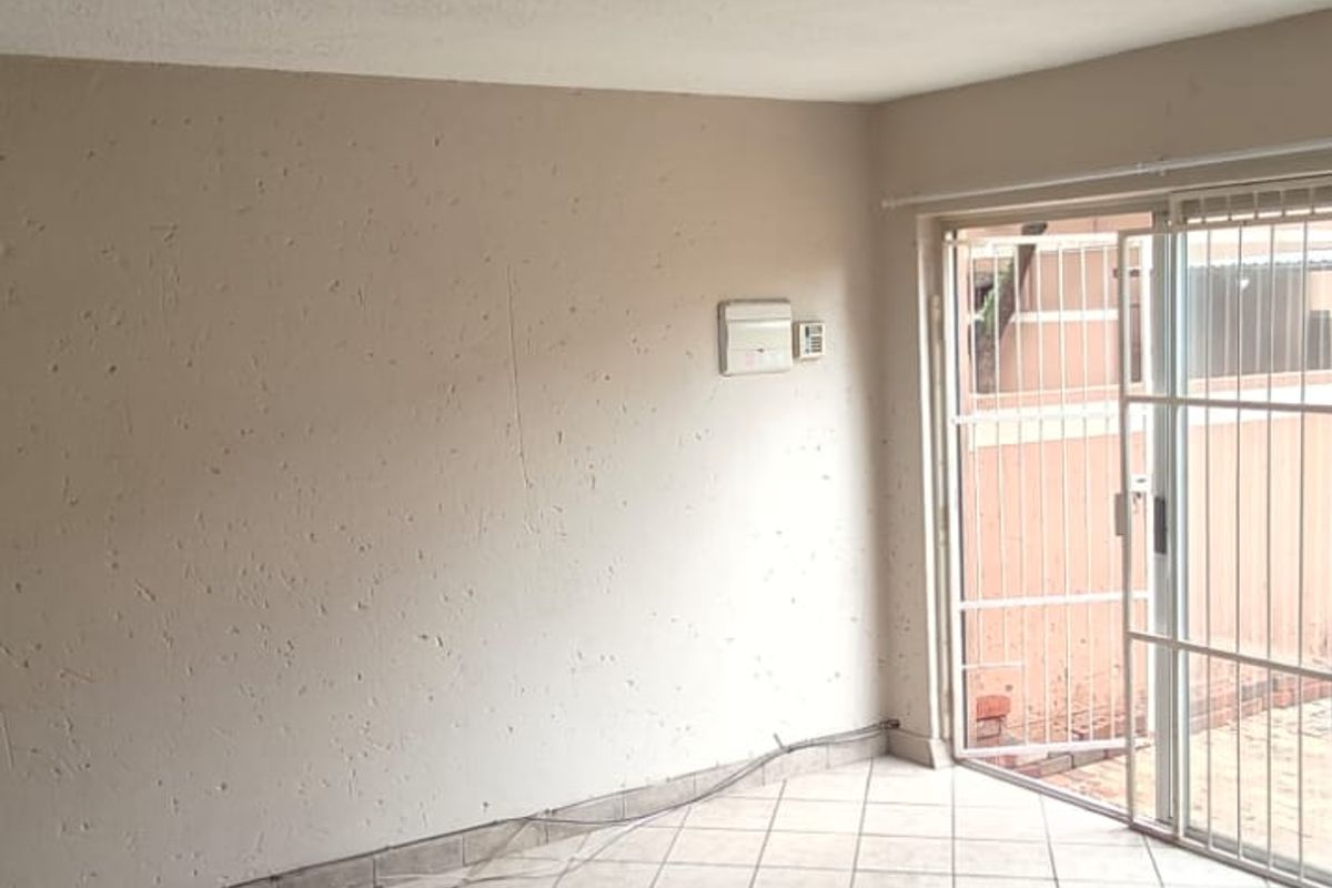 An empty living area featuring tiled flooring, textured ceiling, and sliding glass doors with security gates leading to the exterior.
