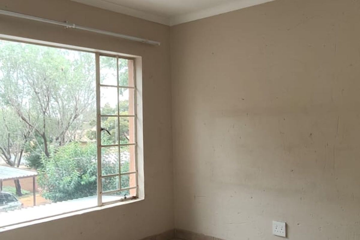 A vacant bedroom featuring neutral tiled flooring, a large window with security bars, and plain wall finishes, ready for a fresh coat of paint.
