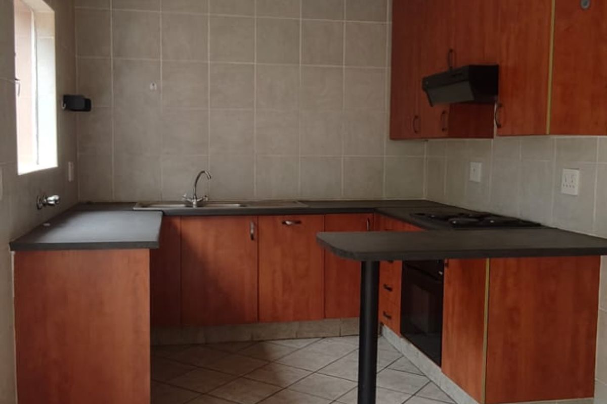 A functional kitchen featuring wood-look cabinetry, dark countertops, a built-in oven, and tiled flooring throughout.