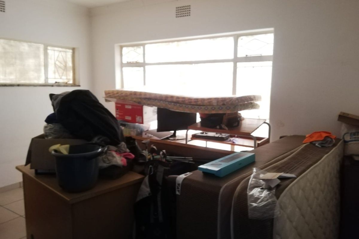 A bedroom space featuring large windows and tiled flooring, currently used for storage.