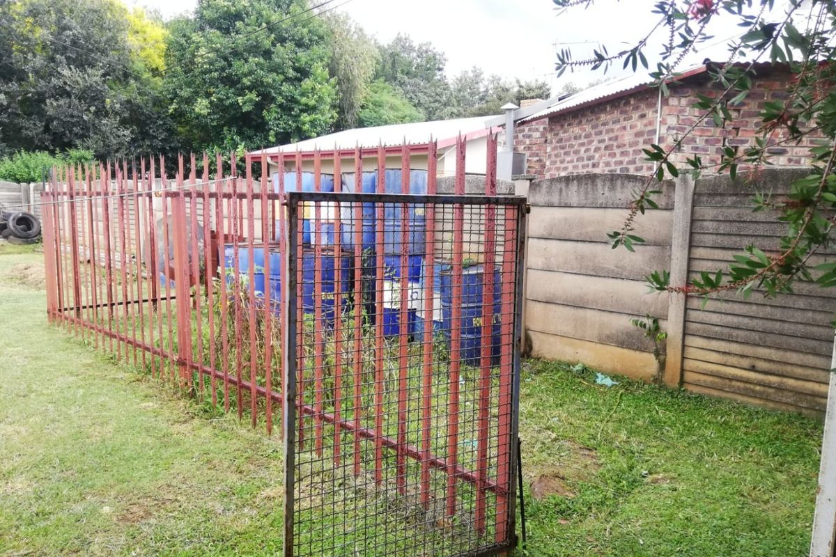 A rear garden area featuring a metal security fence, boundary wall, and lawn space, currently used for storage.