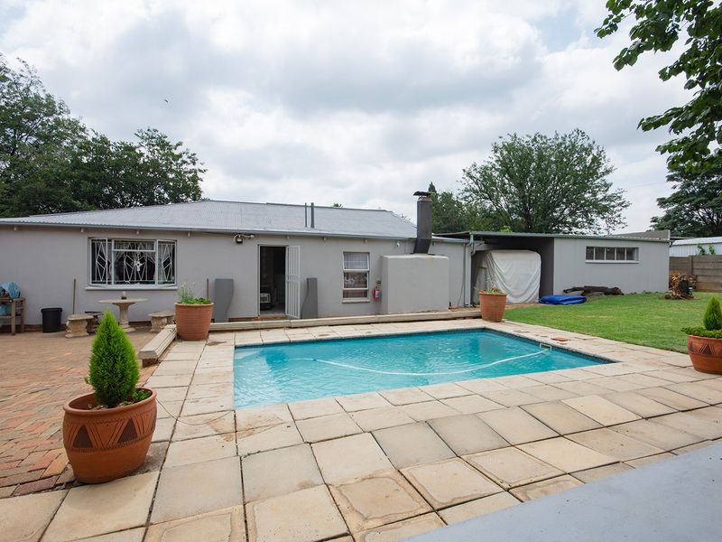 Rear exterior view featuring a swimming pool, paved patio area, and a lawn, providing a functional outdoor space for recreation and relaxation.