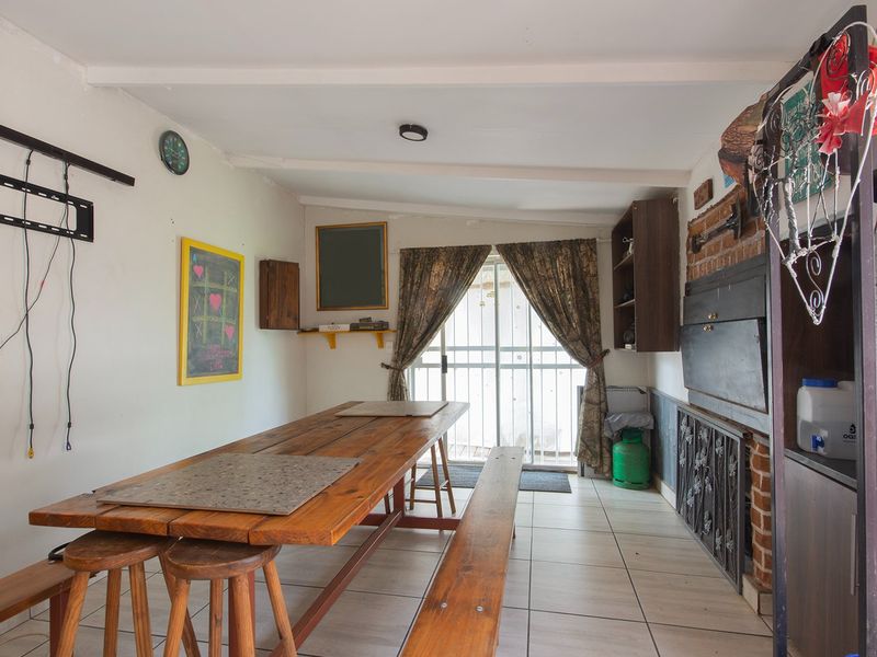 A functional indoor entertainment area featuring tiled flooring, a built-in braai, and direct access to the exterior through a sliding door.