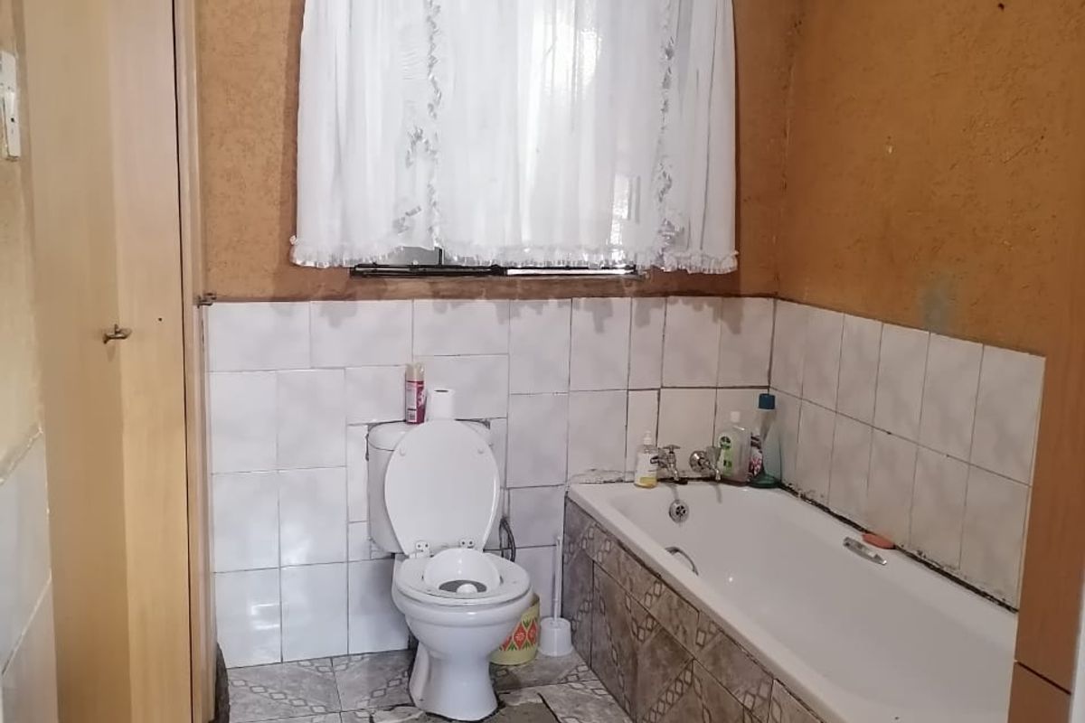 A dated bathroom featuring a standard bathtub, toilet, tiled flooring, and partially tiled walls with a textured finish.