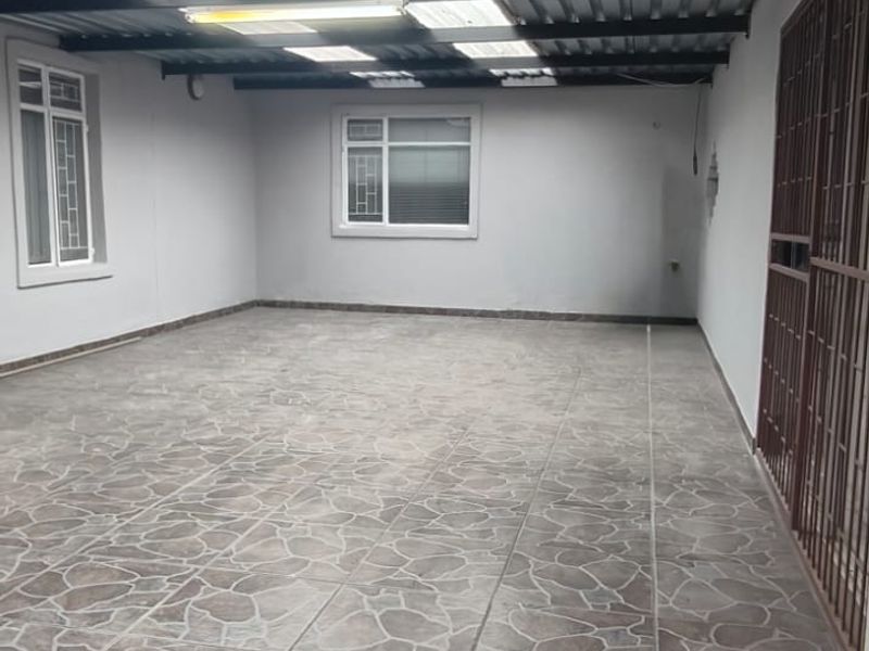 A spacious covered patio area featuring tiled flooring, a corrugated metal roof with translucent panels, and secure metal gate access.