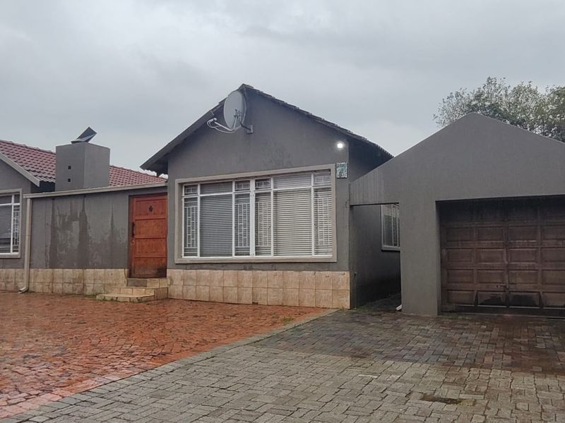 Front elevation of a single-story house featuring a paved driveway, attached garage, and tiled roof under an overcast sky.