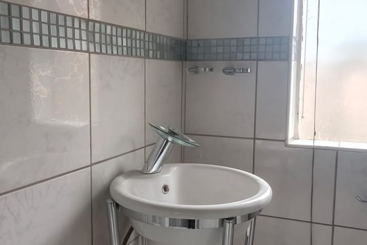 A small bathroom featuring a pedestal basin with chrome faucet, tiled walls with a mosaic border, and a window for natural light.