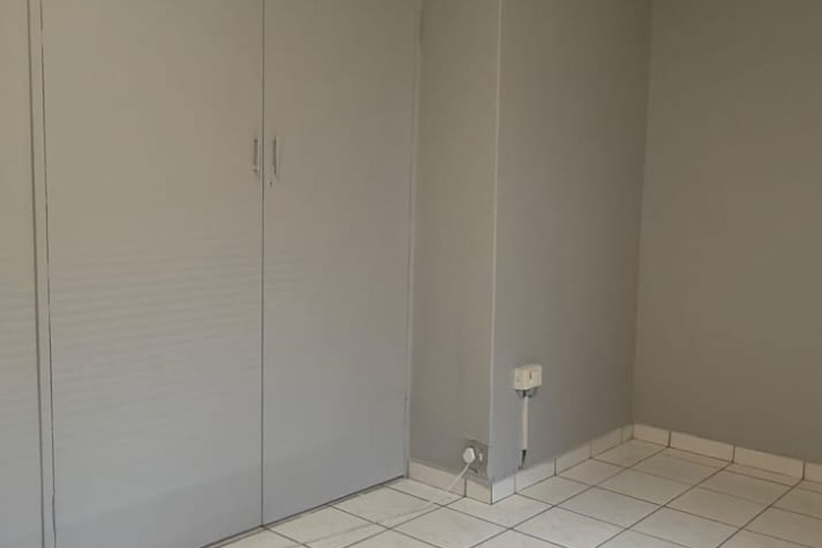 A clean, empty bedroom featuring neutral grey walls, white tiled flooring, and built-in cupboards with recessed ceiling lighting.