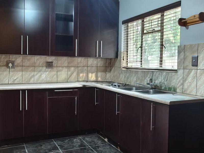 A functional kitchen featuring dark wood cabinetry, tiled backsplash, and dark floor tiles, offering a clean and practical workspace.