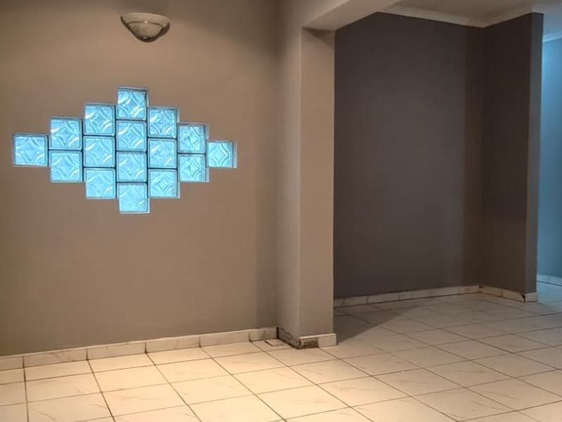 An empty living area featuring neutral grey walls, ceramic floor tiles, and a decorative glass block feature window.