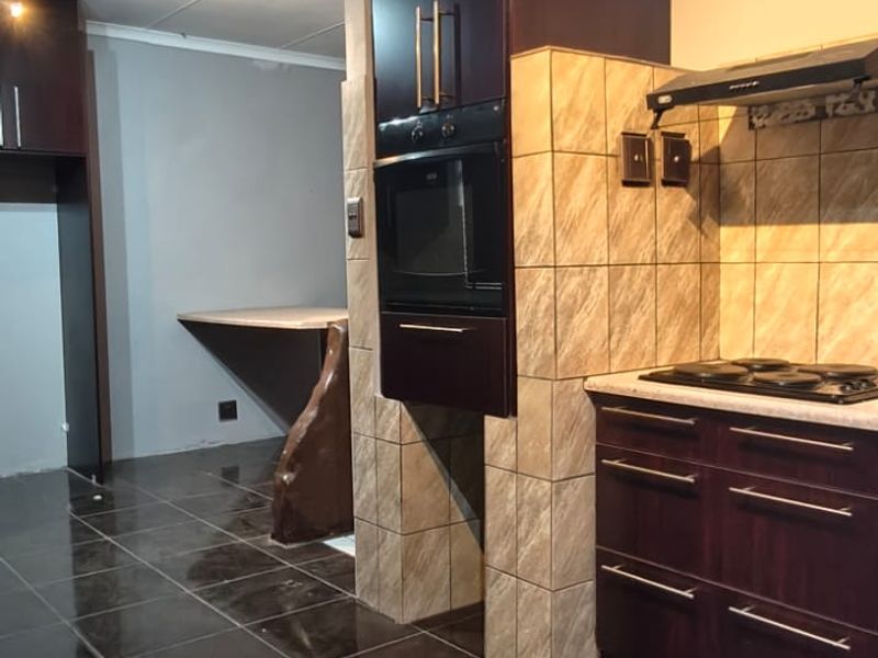 A functional kitchen featuring dark wood cabinetry, built-in oven, hob with extractor fan, tiled backsplash, and dark tiled flooring.