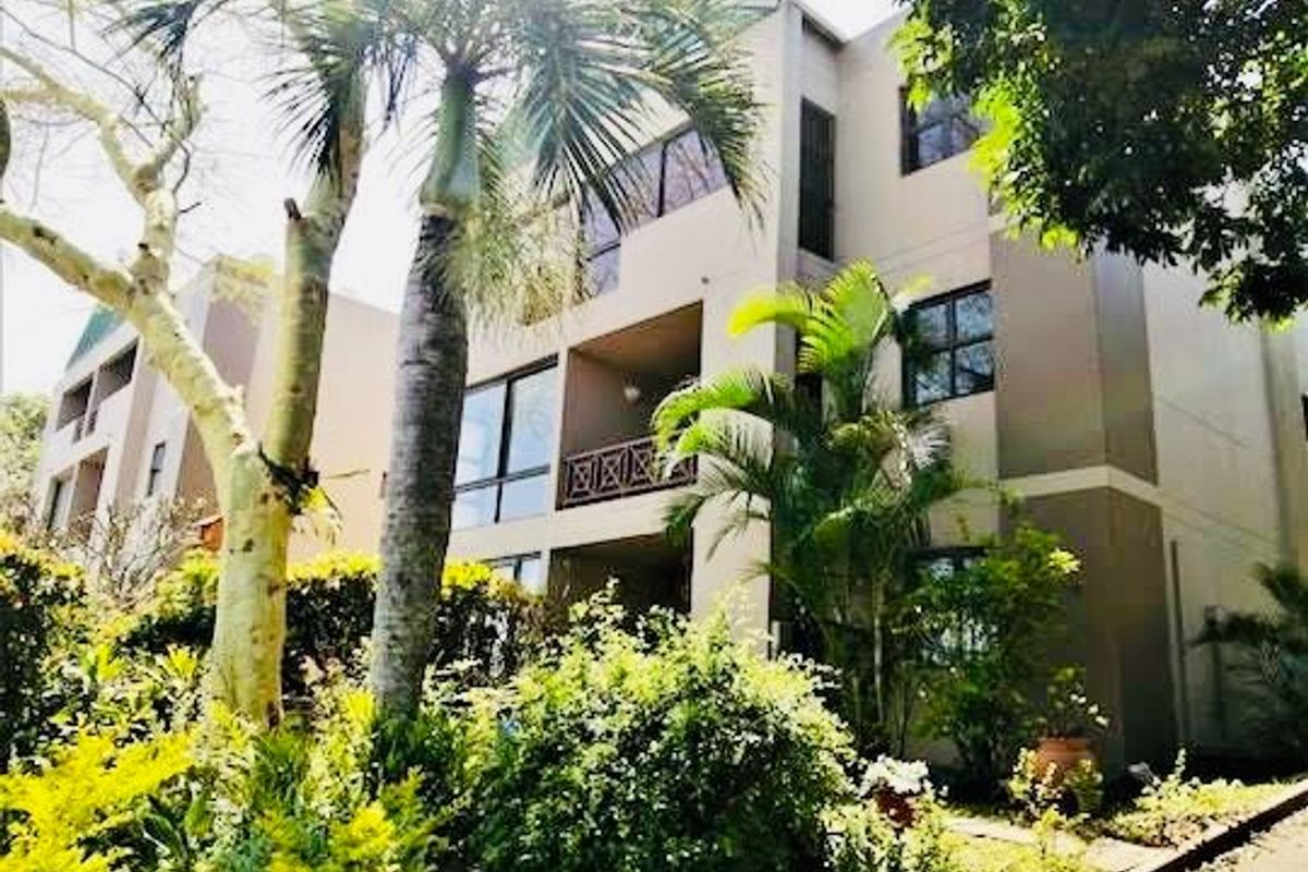 A view of the rear facade of the apartment building, featuring balconies with railings and established garden landscaping.