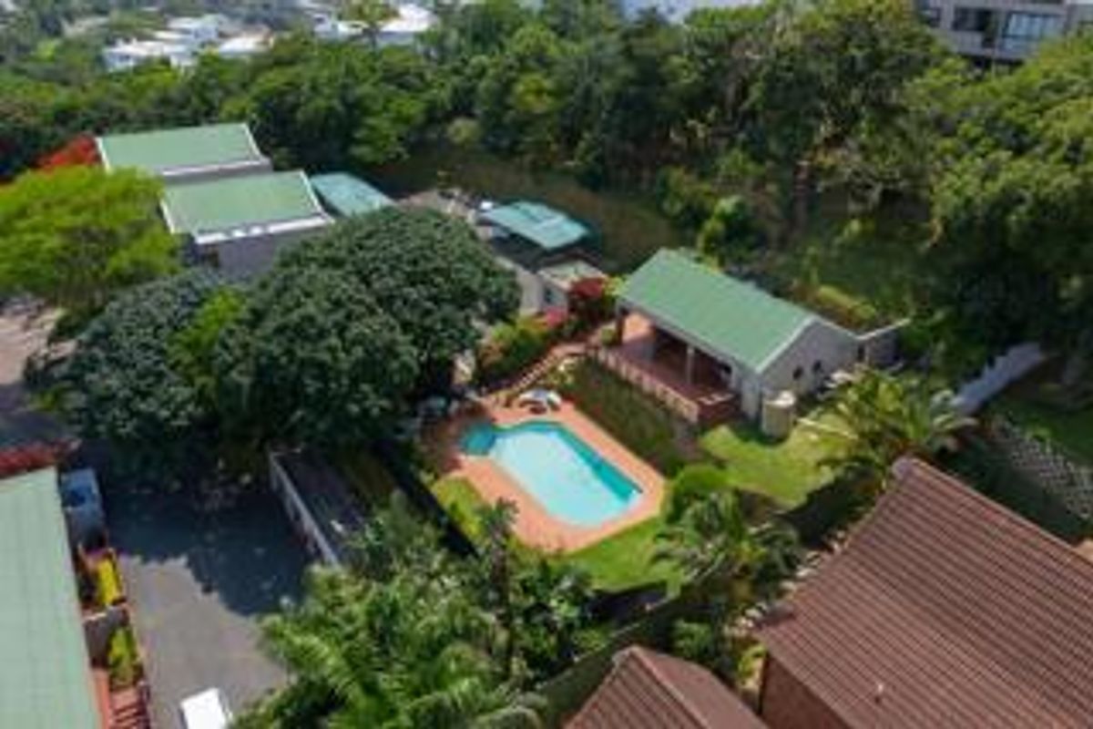 Aerial view of a residential property featuring a swimming pool, landscaped garden, paved driveway, and multiple structures with pitched roofs.