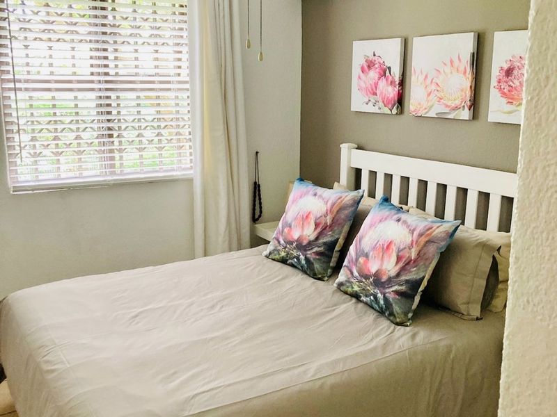 A cozy bedroom featuring tiled flooring, a ceiling fan, and a wall-mounted split-system air conditioner for climate control.