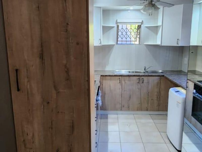 A functional kitchen featuring wood-look cabinetry, tiled flooring, a double sink, and a ceiling fan, offering a practical layout for daily use.