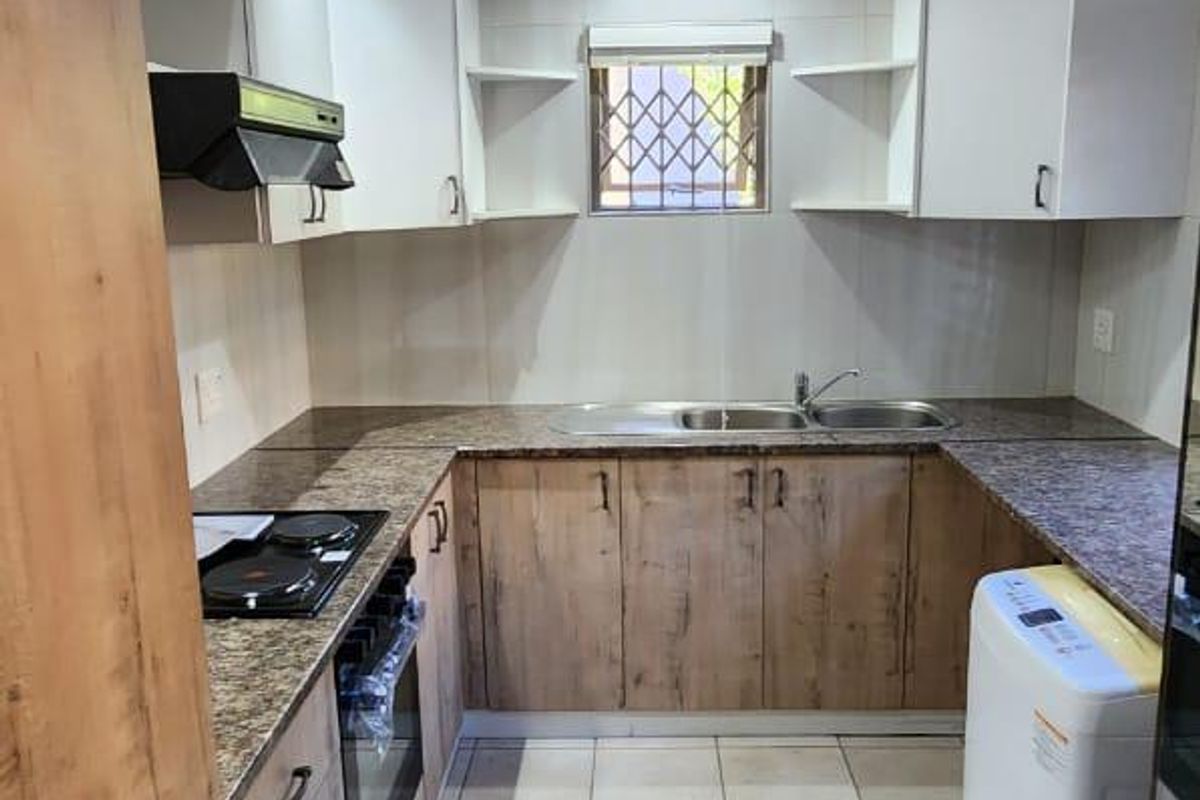 A functional kitchen featuring wood-look cabinetry, granite countertops, a built-in oven, electric hob, and a double basin sink with a security-gated window.