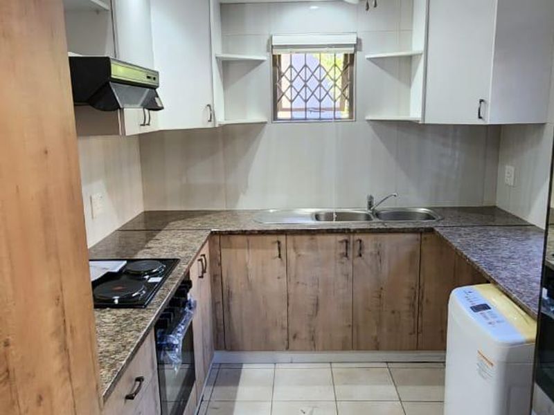 A functional kitchen featuring wood-look cabinetry, granite countertops, a built-in oven, electric hob, and a double basin sink with a security-gated window.