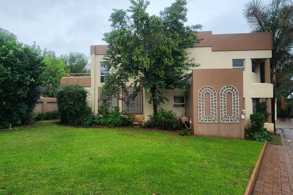 A view of the rear exterior of the two-story house, featuring a well-maintained lawn, paved driveway, and established garden landscaping.