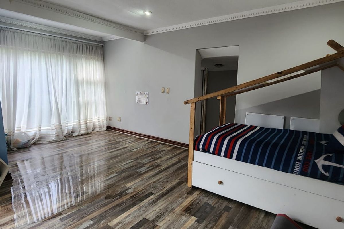 A bedroom featuring laminate flooring, crown molding, and large windows with curtains, offering a functional space with potential for cosmetic updates.