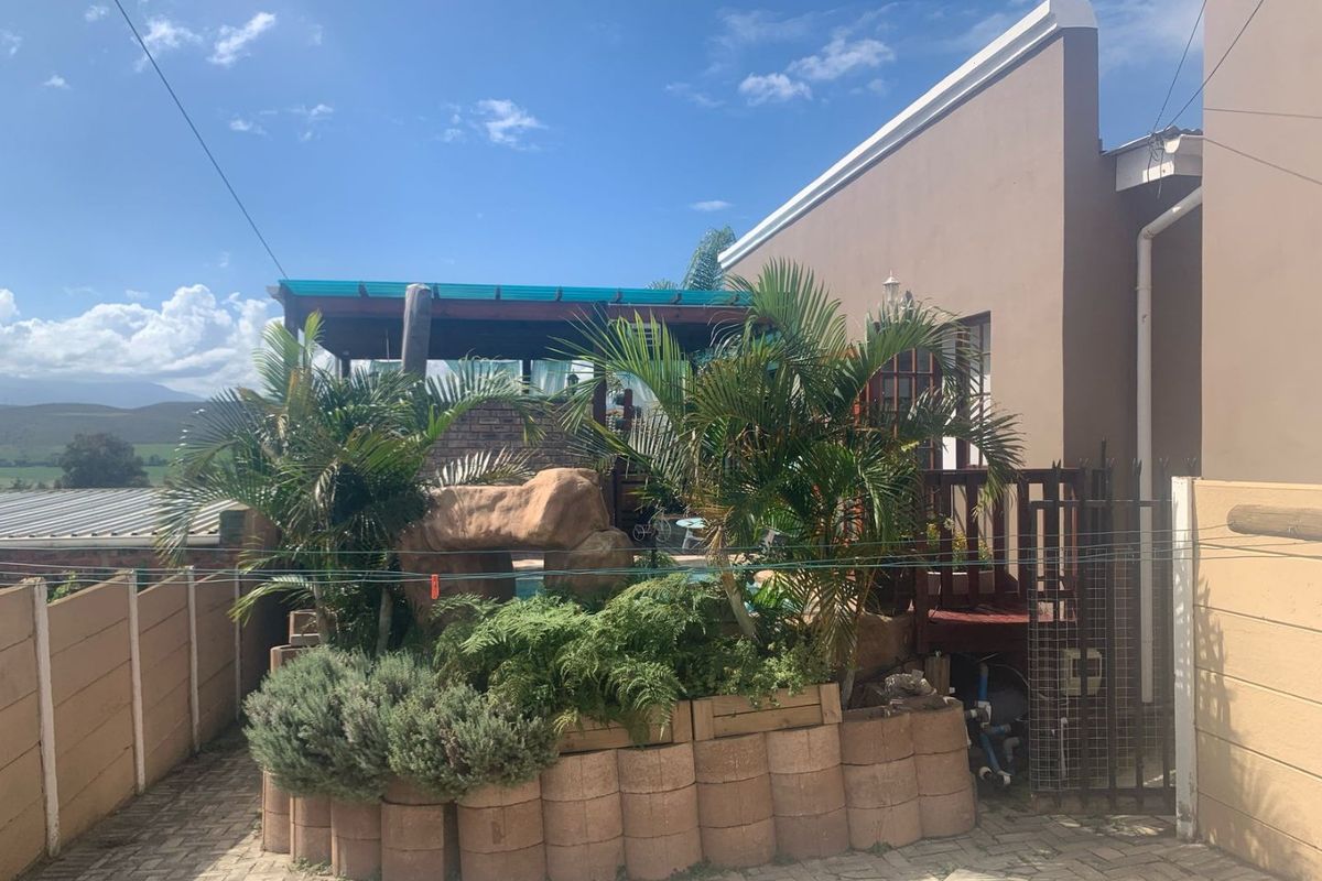A rear garden area featuring a swimming pool, a raised rockery garden bed, and a covered patio structure with timber decking.