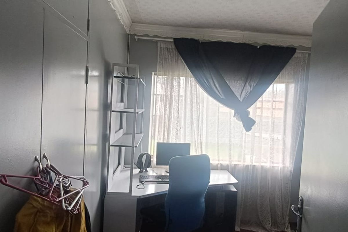A functional bedroom or home office space featuring built-in cupboards and natural light through a window with curtain fixtures.