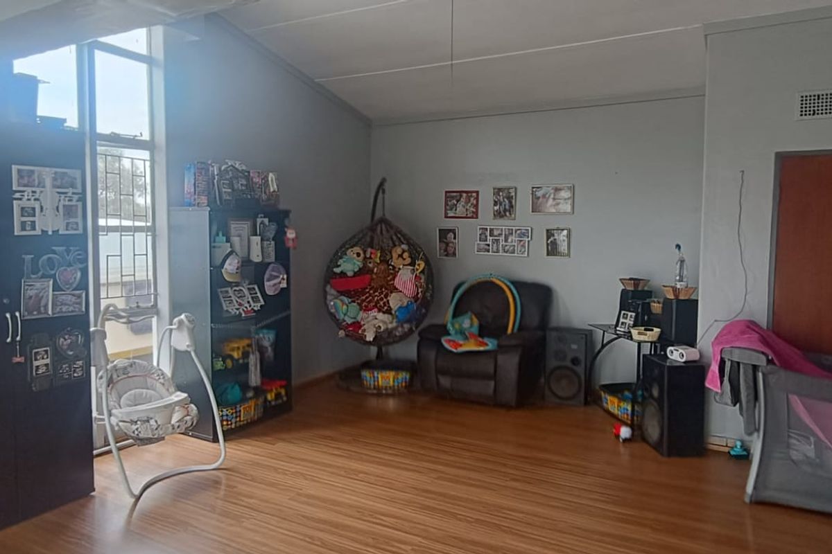 A spacious living area featuring laminate flooring, high ceilings, and large windows that provide ample natural light.