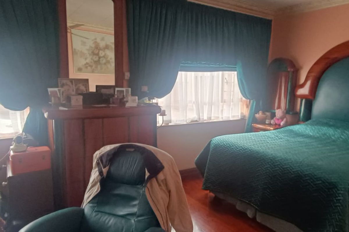 A bedroom featuring traditional wood-framed bed and cabinetry with large windows and heavy drapery.