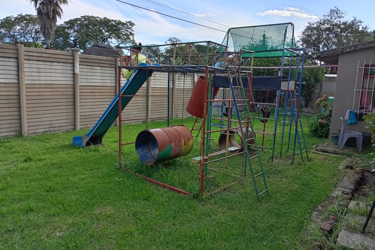A rear garden area featuring a large metal playground structure with a slide and climbing frame, enclosed by a concrete perimeter wall.