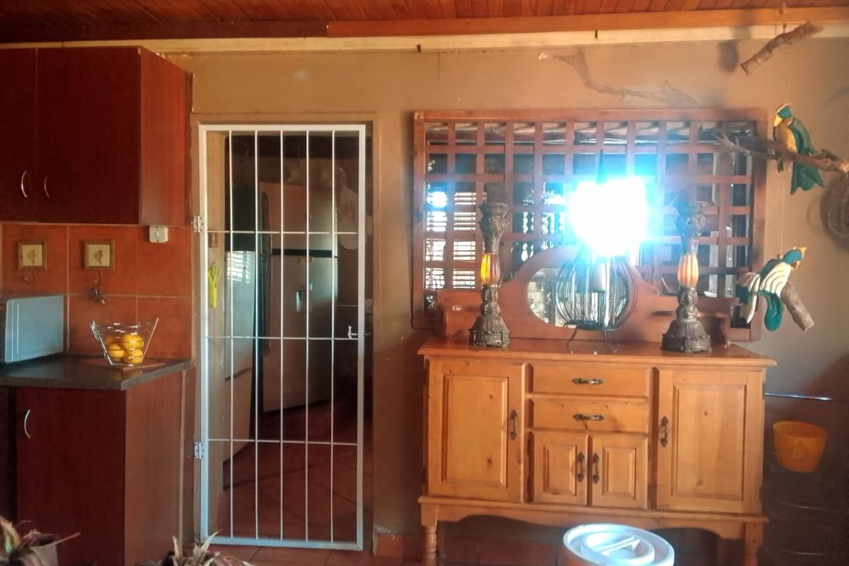A rustic kitchen area featuring dark wood cabinetry, tiled splashbacks, and a security gate leading to an adjacent utility space with a timber ceiling.